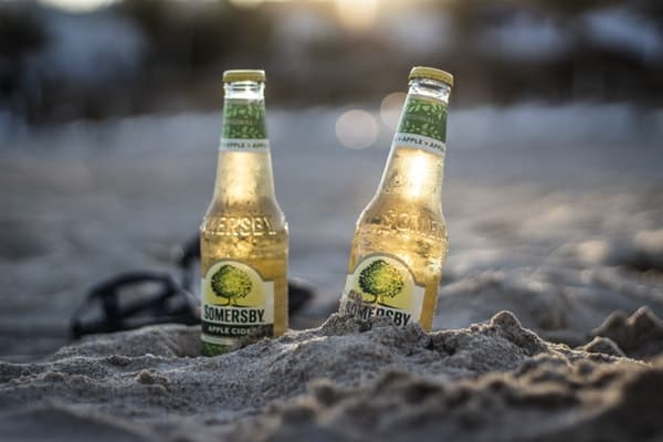 two bottles of apple cider half buried in the sand