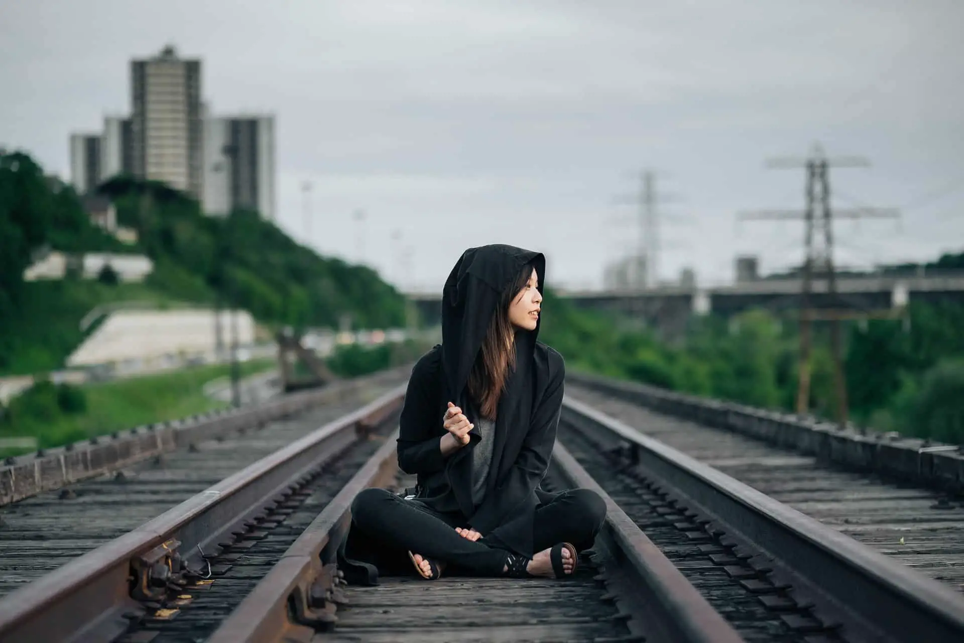 Hipster wearing a black hoodie jacket is sitting at the center of rail road